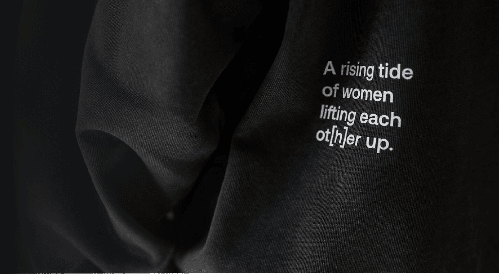 Detailaufnahme eines dunklen Sweatshirts mit weißem Schriftzug „A rising tide of women lifting each ot[h]er up.“