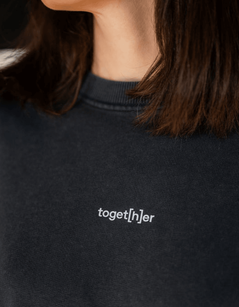 Detailaufnahme einer Person, die schwarzen Sweater mit Schriftzug „toget[h]er“ auf der Brust trägt