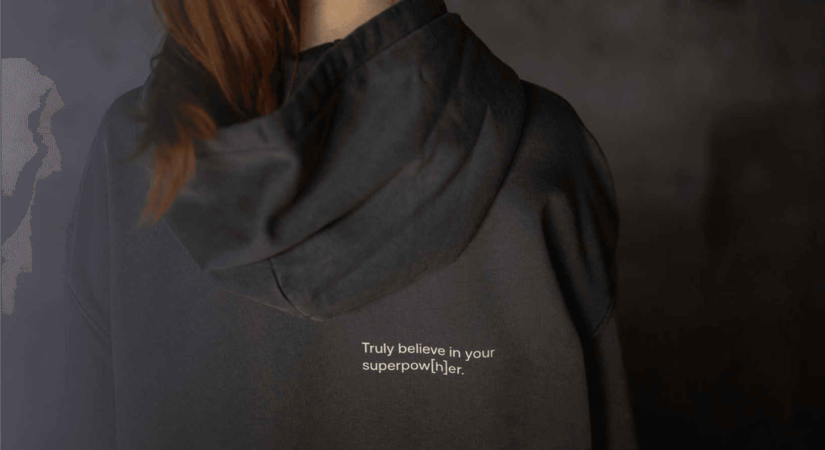 Detailaufnahme einer Person, die einen dunkelgrauen Sweater mit Schriftzug auf dem Rücken trägt