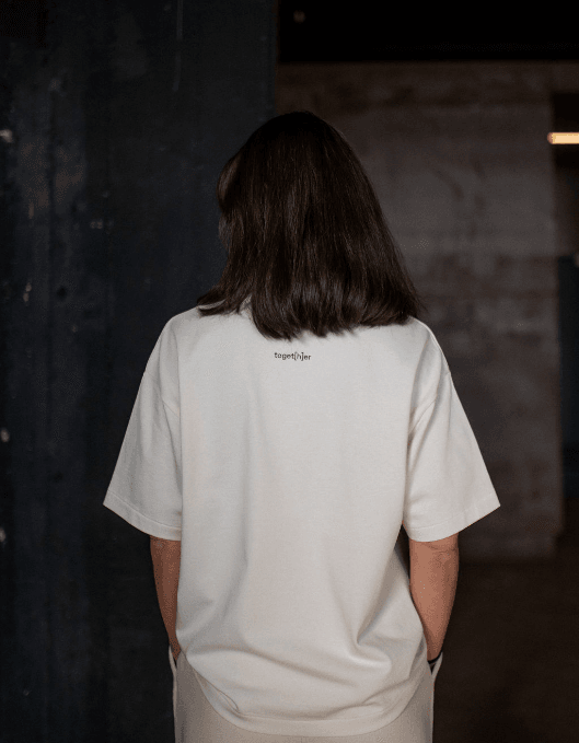 Person trägt helles T-Shirt mit einem kleinen Logo toget[h]er oben mittig auf dem Rücken