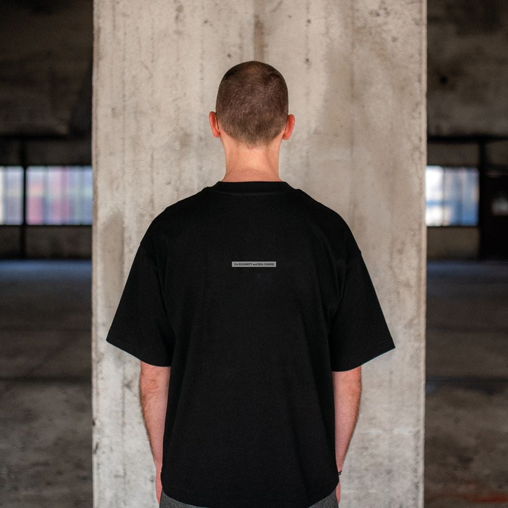 Person trägt schwarzes T-Shirt mit Schriftzug „For solidarity and real change“ auf dem Rücken