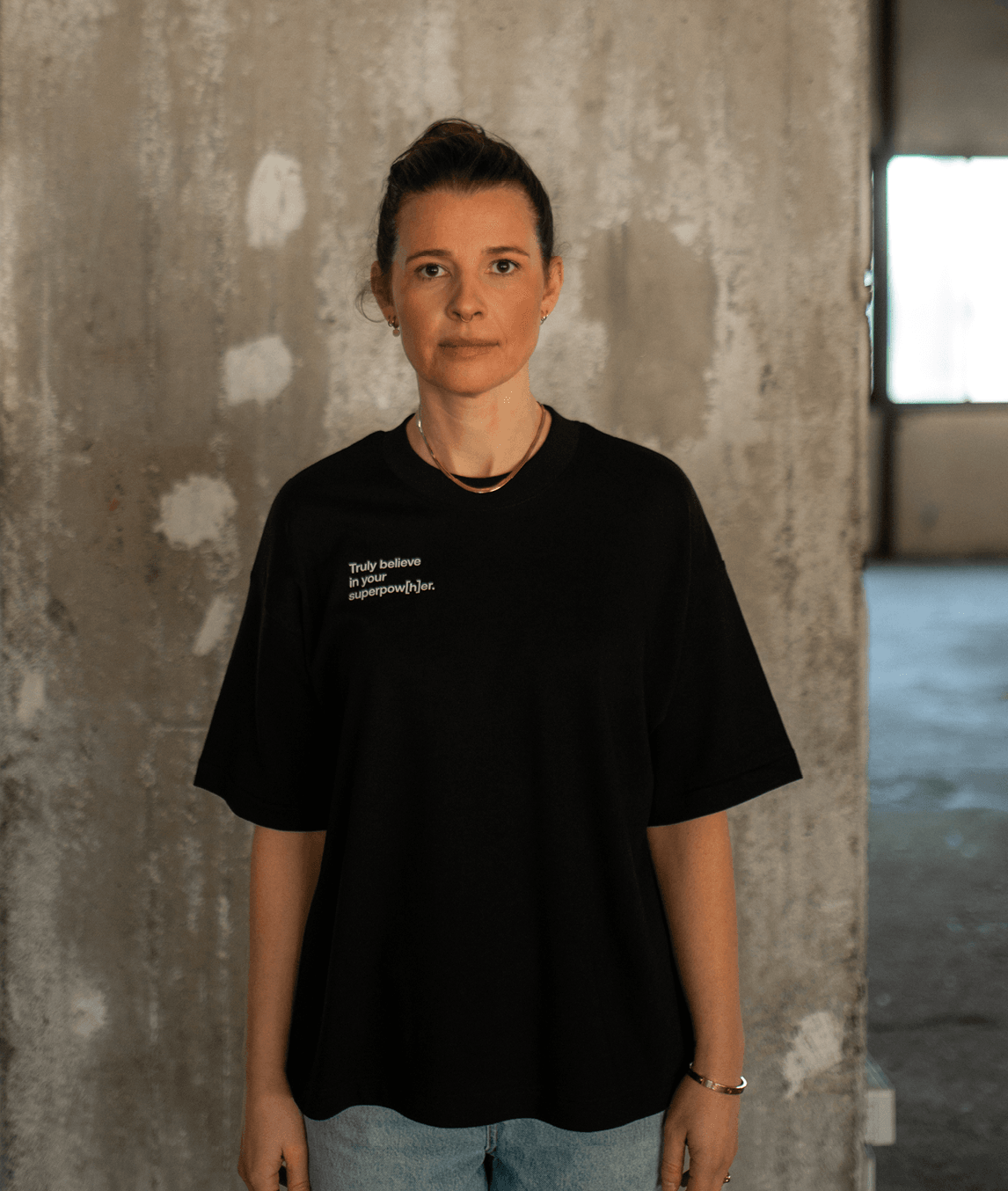 Frau trägt schwarzes T-Shirt mit Schriftzug „Truly believe in your superpow[h]er“ rechts auf der Brust