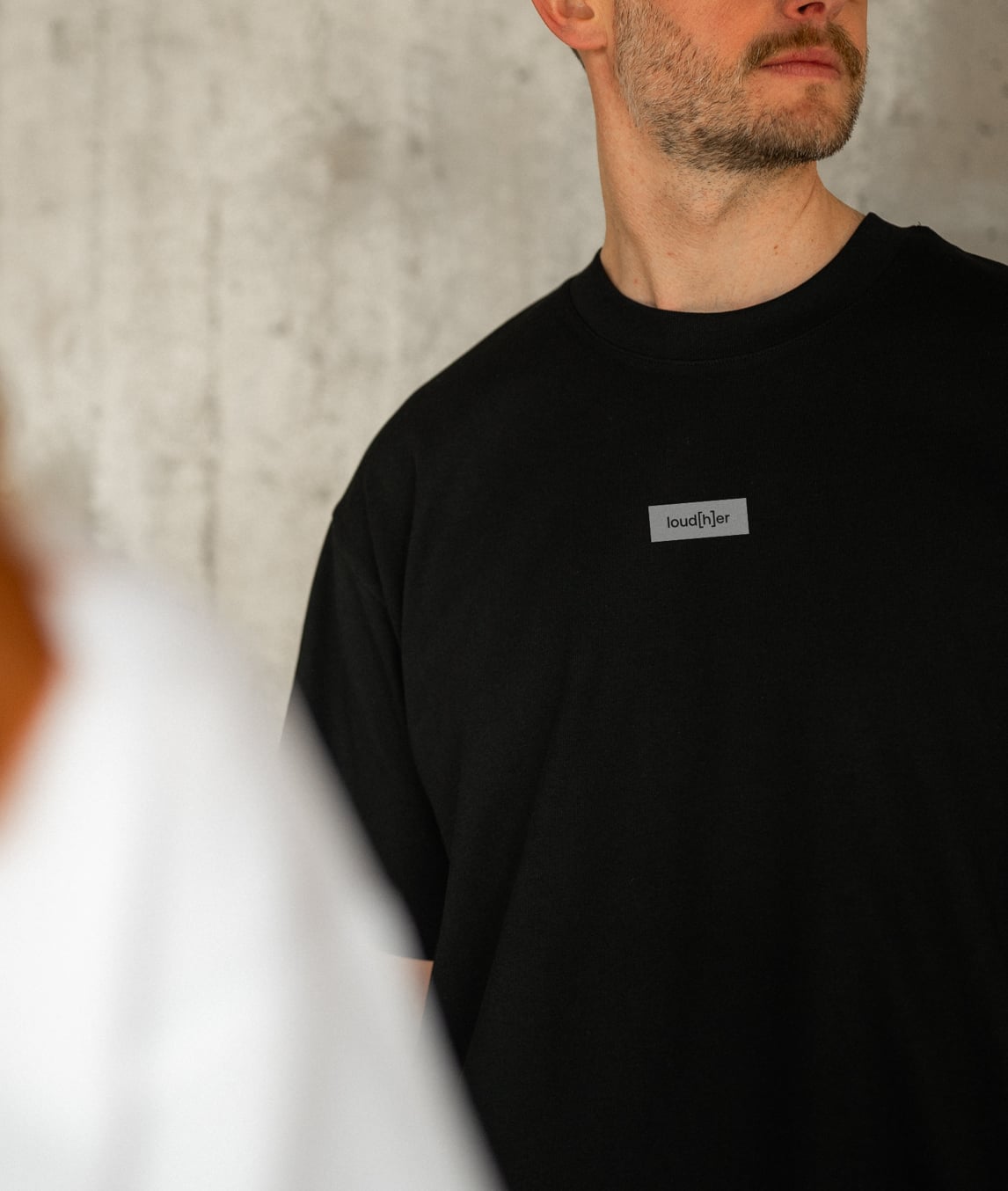 Person trägt schwarzes T-Shirt mit Schriftzug „loud[h]er“ auf der Brust